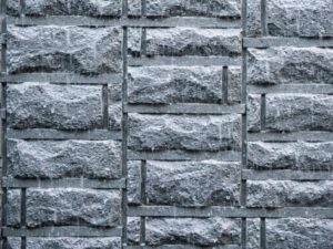 雨が激しく降り注ぐグレーの石積み調タイル外壁