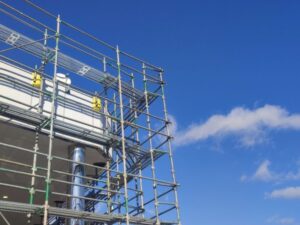 青空を背景に建物の外壁に組まれた金属製の足場を見上げた工事現場